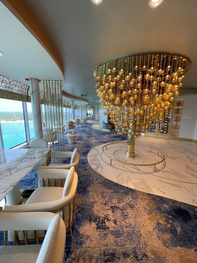 Enchanté's elegant dining room with a dramatic gold bubble chandelier, marble flooring, and ocean-view windows