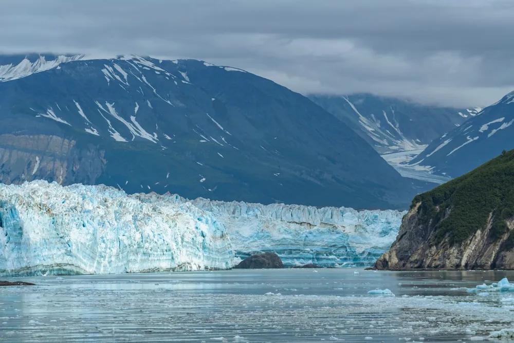 A tidewater glacier meeting the sea in Alaska, ice floating in the channel below snow-streaked mountains